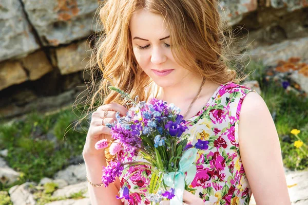 Uma menina em um vestido colorido mantém um buquê de flores silvestres — Fotografia de Stock