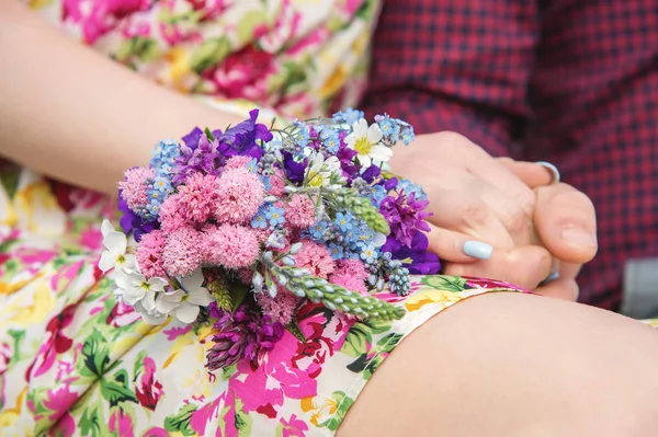 Les jeunes mariés se tiennent la main avec un bouquet qui se trouve sur les genoux des mariées — Photo