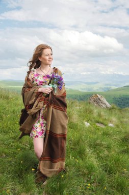 güzel sarışın kız bir ekose sarılmış ve kır çiçekleri buketi ile standları dik dik bakar