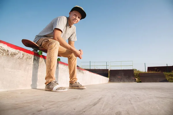 Um adolescente está sentado em um skate no parque e sorrindo — Fotografia de Stock