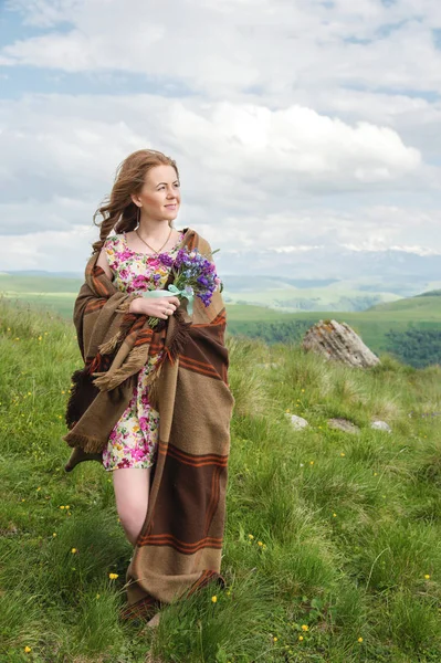 güzel sarışın kız bir ekose sarılmış ve kır çiçekleri buketi ile standları dik dik bakar