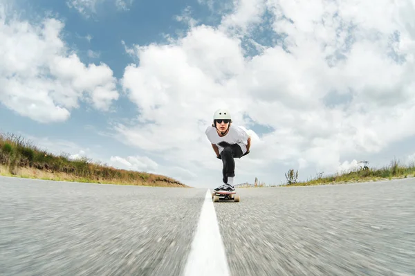 Um tipo com um capacete e óculos de sol está a andar de longboard numa estrada rural. — Fotografia de Stock