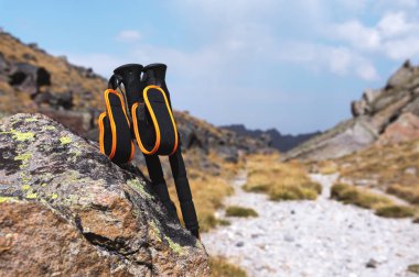 Mavi bir gökyüzü ve beyaz bulutlar karşı yüksek dağ yolu üzerinde bir taş yakınlarında bir dağ tırmanışı için profesyonel sopa.