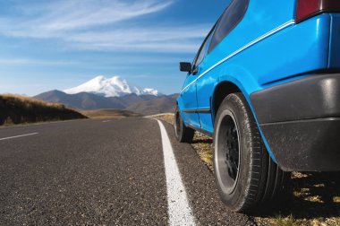 Yol kenarında mavi bir araba ile yüksek dağ manzarası. Kuzey Kafkasya.