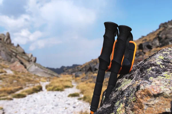 Mavi bir gökyüzü ve beyaz bulutlar karşı yüksek dağ yolu üzerinde bir taş yakınlarında bir dağ tırmanışı için profesyonel sopa.