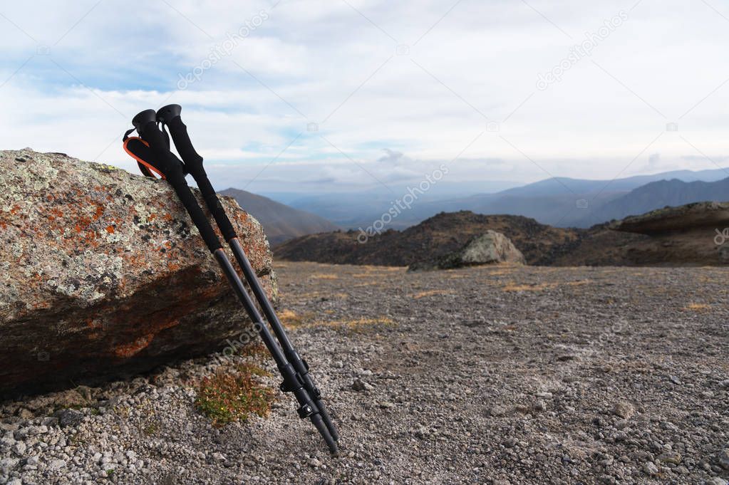 Professional sticks for climbing a mountain near a stone on a high mountain path against a blue sky and white clouds.