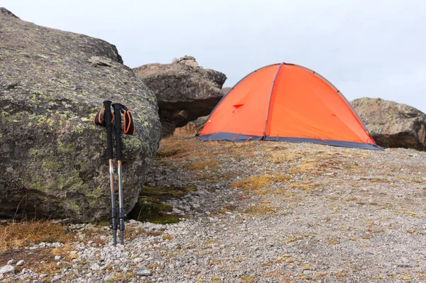 Trekking mountain sticks stand near a stone near the orange trekking tent on the deserted stone slopes of the elbrus