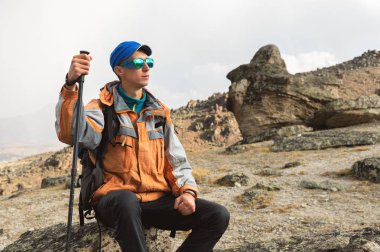 Güneş gözlüğü ve bir sırt çantası ile yalnız bir turist bir kayaya oturmuş dinleniyor