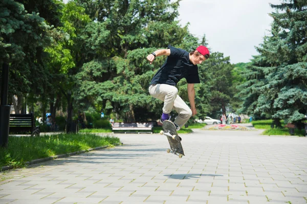 Langhaariger Skater-Teenager in T-Shirt und Turnschuhmütze springt eine Gasse gegen einen stürmischen Himmel — Stockfoto