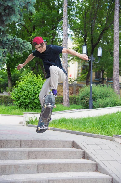 Długowłosy nastolatek skater w T-shirt i czapkę sneaker skacze aleja przeciwko burzliwe niebo — Zdjęcie stockowe