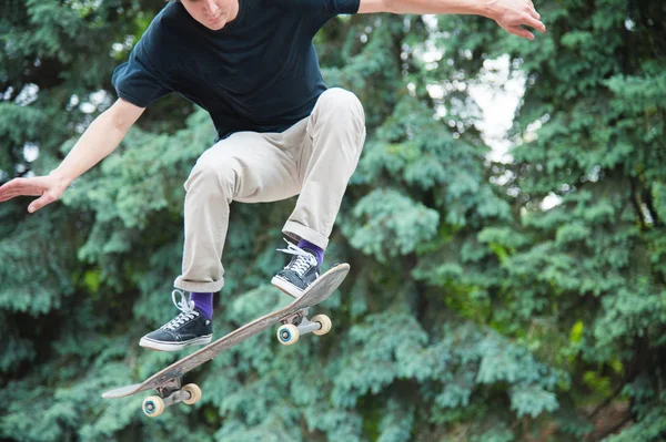 Pelo largo skater-adolescente en una camiseta y una zapatilla de deporte sombrero salta un callejón contra un cielo tormentoso — Foto de Stock