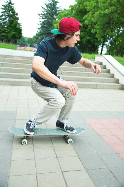 Patinador de cabelos compridos adolescente em uma camiseta e um chapéu de sapatilha salta um beco contra um céu tempestuoso — Fotografia de Stock