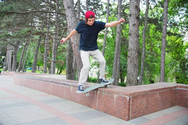 Pelo largo skater-adolescente en una camiseta y una zapatilla de deporte sombrero salta un callejón contra un cielo tormentoso — Foto de Stock