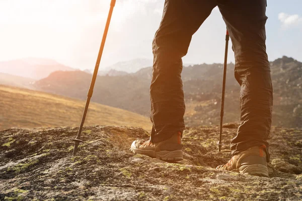 Close-up de pernas masculinas em botas de trekking com paus para caminhada nórdica contra o fundo de rochas e distantes terras caucasianas — Fotografia de Stock