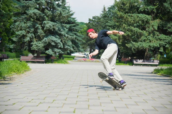 Langhaariger Skater-Teenager in T-Shirt und Turnschuhmütze springt eine Gasse gegen einen stürmischen Himmel — Stockfoto