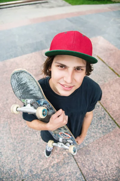 Um jovem patinador fica com um skate no fundo da paisagem da cidade — Fotografia de Stock