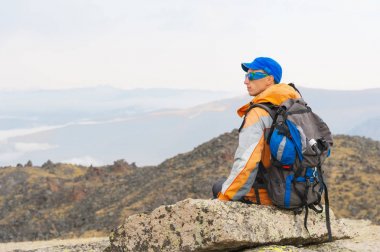 Güneş gözlüğü ve bir sırt çantası ile yalnız bir turist bir kayaya oturmuş dinleniyor