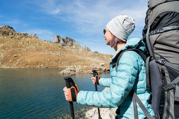 Bir uzun yürüyüşe çıkan kimse kız güneş gözlüğü ve şapka onun elinde Treklerimiz izleme ile bir sırt çantası ve dağ dişli ile yüksek dağ gölü Kuzey Kafkasya'da bir adalar güzel manzarasına bakar