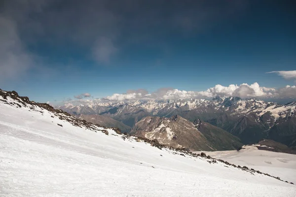Donker blauwe hemel met wolken op de rotsige toppen van de bergen bedekt met gletsjers en sneeuw — Stockfoto