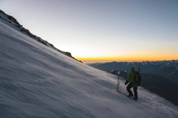 Alpinista ao nascer do sol caminhadas de manhã cedo na encosta e no chão acima da neve varre neve à deriva — Fotografia de Stock
