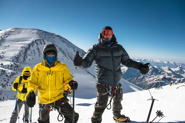 Arkadaşları bir karla kaplı dağın tepesine giderken yanında bir başparmak aşağı bir ceket ve koşum takımı orta yaşlı bir dağcı ortaya — Stok fotoğraf