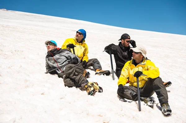 Альпинист в солнечном месте и профессиональное снаряжение, лежащее на снежном склоне в окружении своих товарищей — стоковое фото