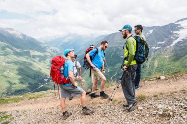 Bir grup yürüyüşçü sırt çantaları ve izleme ile dinlenme sopa ve onların rehber için dinleme dağlarda standları