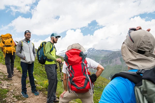 A group of hikers with backpacks and tracking sticks rest and stands in the mountains listening to their guide