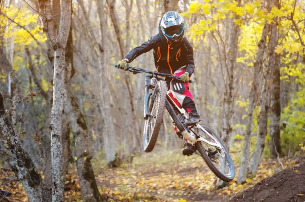 Un giovane cavaliere al volante della sua mountain bike fa un trucco nel saltare sul trampolino del sentiero in discesa nel bosco autunnale — Foto Stock