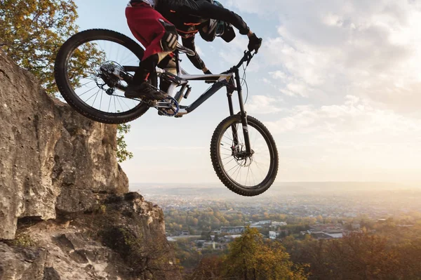 Un jinete joven al volante de su bicicleta de montaña hace un truco en saltar en el trampolín del camino de montaña cuesta abajo en el bosque de otoño —  Fotos de Stock