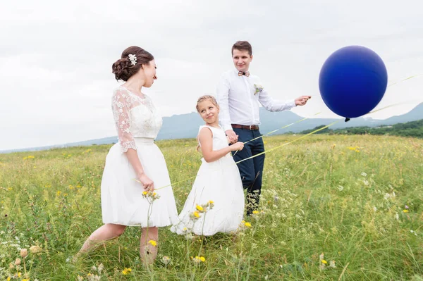 Una giovane coppia e la loro figlia in abiti da sposa camminano nella natura con palloncini — Foto Stock