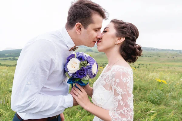 Um par de recém-casados de pé em um abraço de braços na natureza — Fotografia de Stock