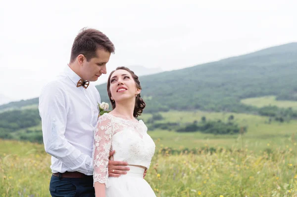 Um par de recém-casados de pé em um abraço de braços na natureza — Fotografia de Stock