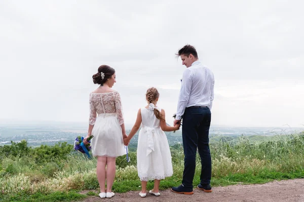 Молода подружня пара і їх маленька дочка в день весілля стоять на природі тримаючи руки — стокове фото
