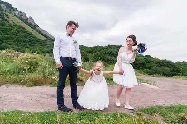 Una joven pareja y su hija en vestidos de novia están caminando en la naturaleza — Foto de Stock
