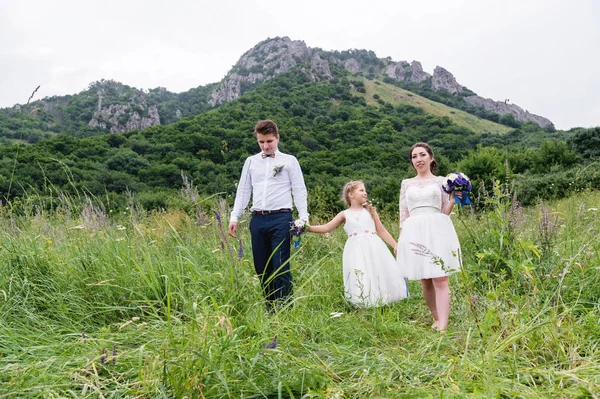 Un jeune couple et leur fille en robes de mariée marchent dans la nature — Photo