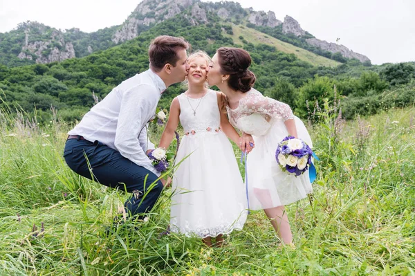 Junge Eltern in Brautkleidern küssen ihre kleine Tochter auf die Wangen — Stockfoto