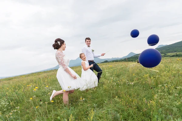 Una giovane coppia e la loro figlia in abiti da sposa camminano nella natura con palloncini — Foto Stock
