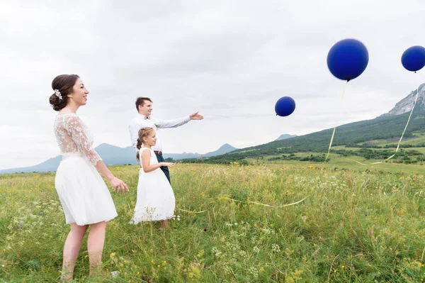 Молода пара і їх дочка у весільних сукнях ходять на природі з повітряними кулями — стокове фото