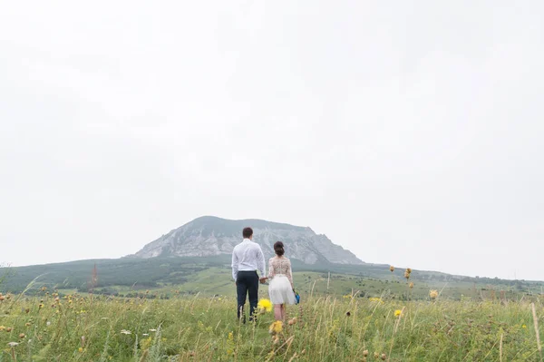 Um par de recém-casados de pé em um abraço de braços na natureza — Fotografia de Stock