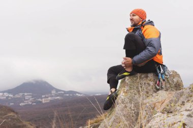 Hipster - dagci aşağı bir ceket ve örme kap oturur ve bir kayanın üstünde duruyor