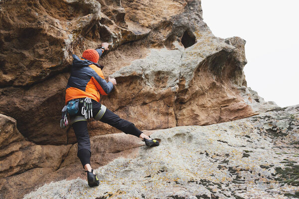 Hipster - climber at the age of climbing up a beautiful rock without insurance and helmet