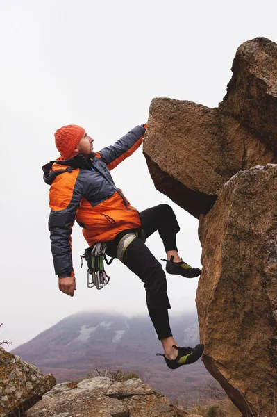 Hipster - klimmer opknoping aan de ene kant op een rots tegen de achtergrond van de Kaukasische bergen in de late herfst. — Stockfoto
