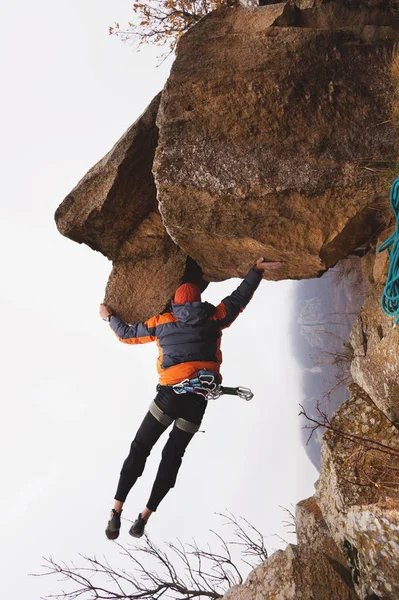 在深秋高加索山脉的映衬下, 一只手悬在岩石上的时髦的登山者. — 图库照片