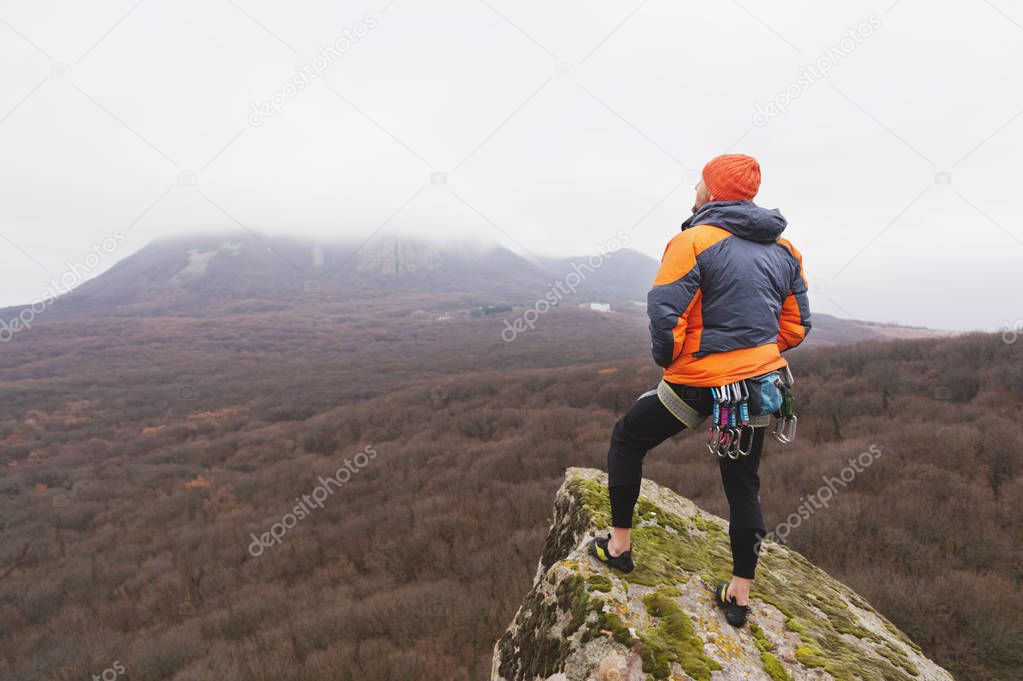Hipster - a climber in a down jacket and a knitted cap stand and rests on the top of a rock