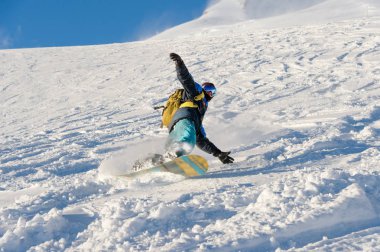 Freeride snowboard kar toz mavi gökyüzüne karşı geride bırakarak bir karla kaplı yamaç rulo