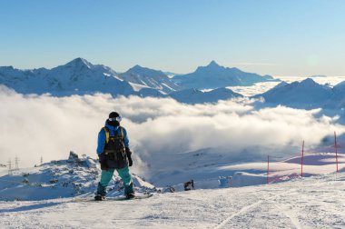 Bir sırt çantası ile profesyonel bir snowboard alçak bulutlar ve Kafkas Dağları arka planı dağlarda kar yüksek üzerinde batan güneşin sırasında duruyor