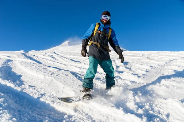 Freeride snowboarder ρολά σε μια πλαγιά χιονισμένη αφήνοντας πίσω μια σκόνη χιόνι ενάντια στον γαλάζιο ουρανό — Φωτογραφία Αρχείου