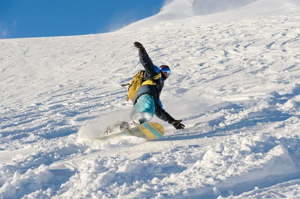 Freeride snowboarder ρολά σε μια πλαγιά χιονισμένη αφήνοντας πίσω μια σκόνη χιόνι ενάντια στον γαλάζιο ουρανό — Φωτογραφία Αρχείου