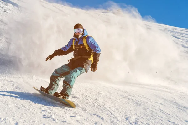 Freeride snowboarder rueda sobre una pendiente cubierta de nieve dejando un polvo de nieve contra el cielo azul — Foto de Stock